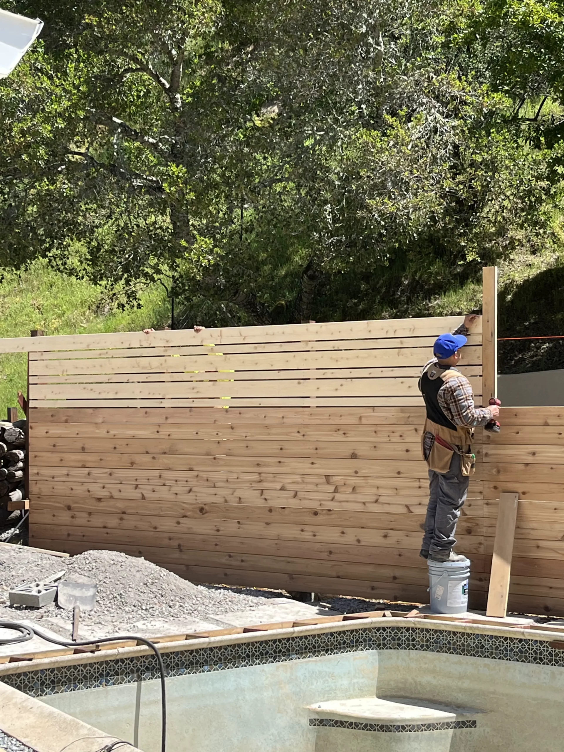 A man is working on a wooden fence near a pool.